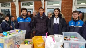 Club staff stand behind a collection of groceries laid out on a table